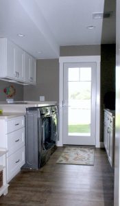 Glass entry door with laundry cabinets and appliances on left hand side